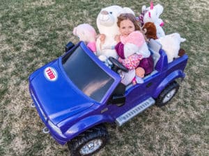 photo of child in power wheels with lots of stuffed animals