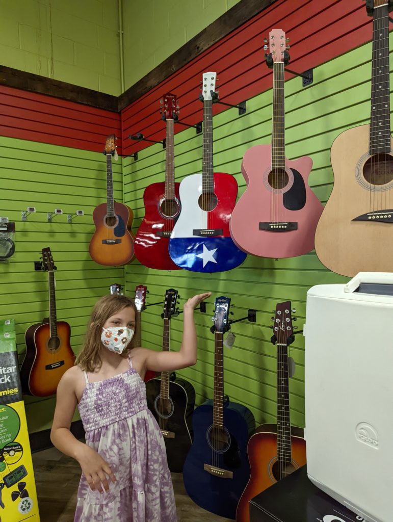 Ada pointing at a pink guitar hanging on the wall in a store