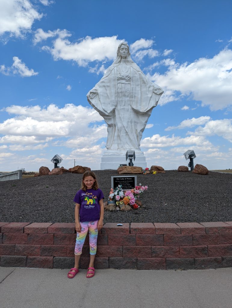 photo of Ada standing in front of marian statue on side of I80